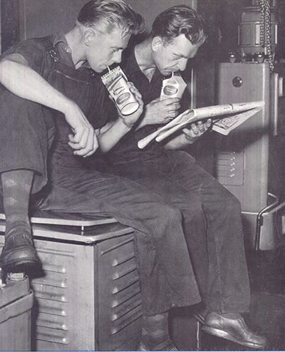 Schwarz-Weiß-Foto von zwei Arbeitern, die aus Perga-Packungen trinken
