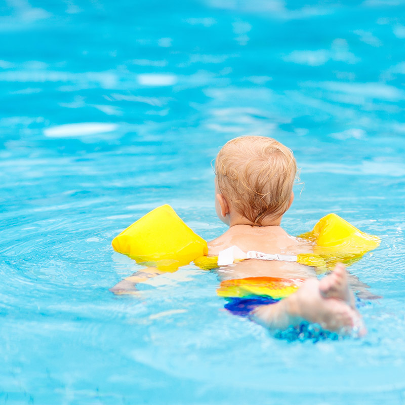 Kleinkind mit Schwimmflügeln im Wasser  